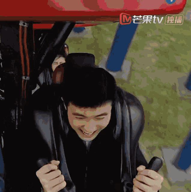 a man is smiling while riding a roller coaster with a tv logo behind him