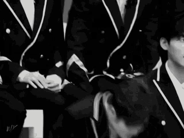 a black and white photo of a group of young men in suits dancing .