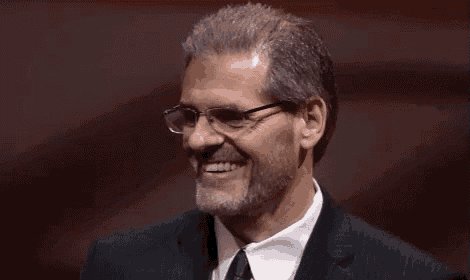 a man with glasses and a beard is smiling in a suit and tie .