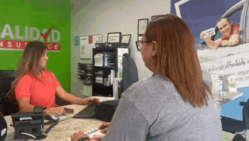 a woman is talking to another woman in front of a sign that says alidad insurance
