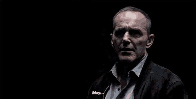 a man in a black jacket and tie is standing in the dark and talking .