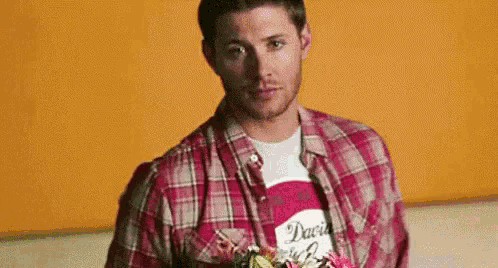 a man wearing a plaid shirt and a t-shirt is holding a bouquet of flowers .