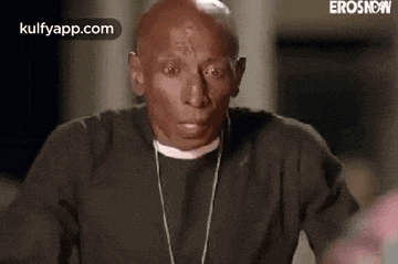 a bald man wearing a black shirt and a chain around his neck is making a funny face .
