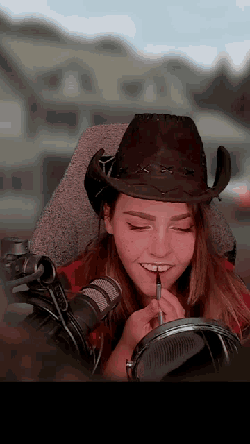 a woman wearing a cowboy hat is smiling and applying lipstick