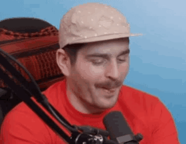 a man with a mustache is wearing a hat and talking into a microphone .