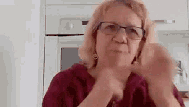 a woman wearing glasses and a red shirt is sitting in a kitchen .