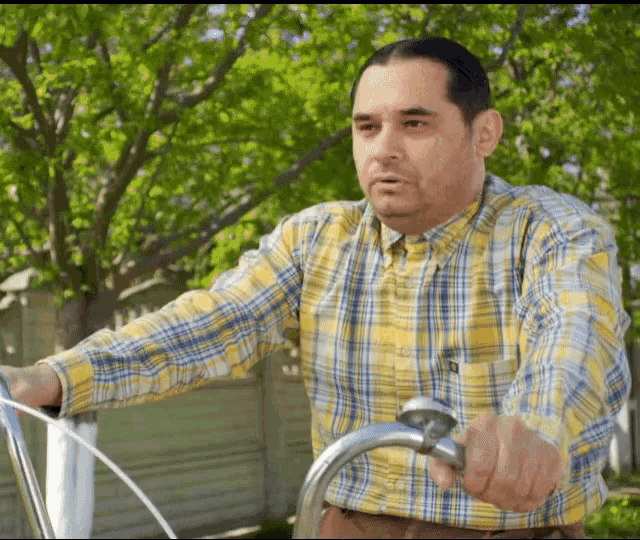 a man wearing a yellow plaid shirt is riding a bike