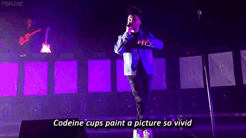 a man singing into a microphone on a stage with the words " codeine cups paint a picture so vivid " below him .