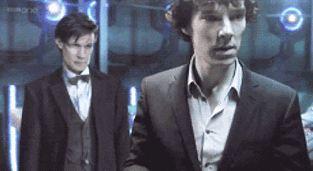 a man in a suit stands next to another man in a suit and bow tie