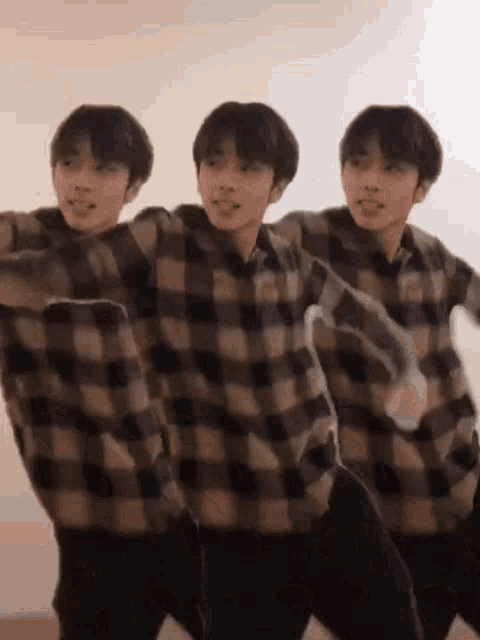 three young men wearing plaid shirts are dancing together .