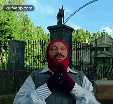 a man wearing a red mask and gloves is standing in front of a statue of a horse .