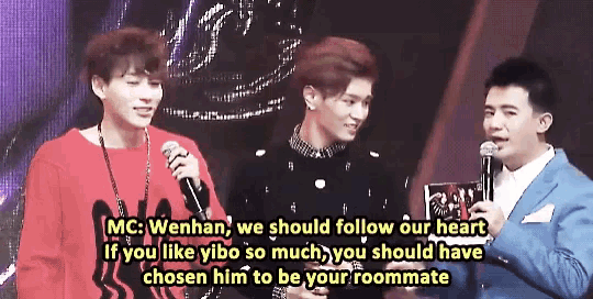 a man in a suit holds a microphone in front of two other men and says mc wenhan we should follow our heart