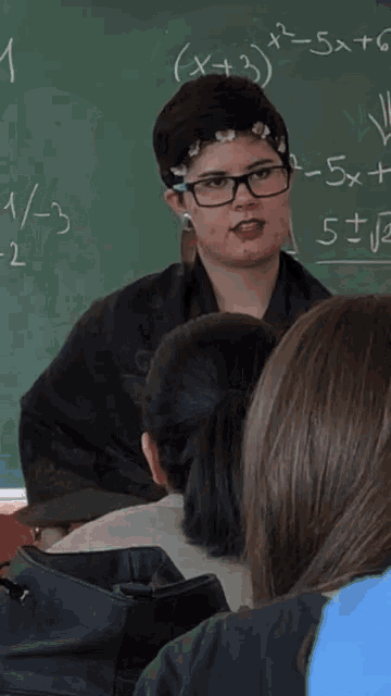 a girl with glasses stands in front of a chalkboard that says x + 3