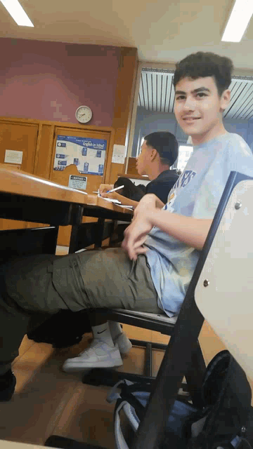 a boy in a tie dye shirt sits at a desk in front of a sign that says no smoking