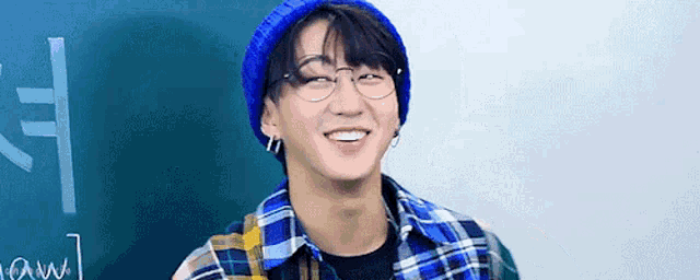 a young man wearing glasses and a plaid shirt is smiling in front of a blackboard .