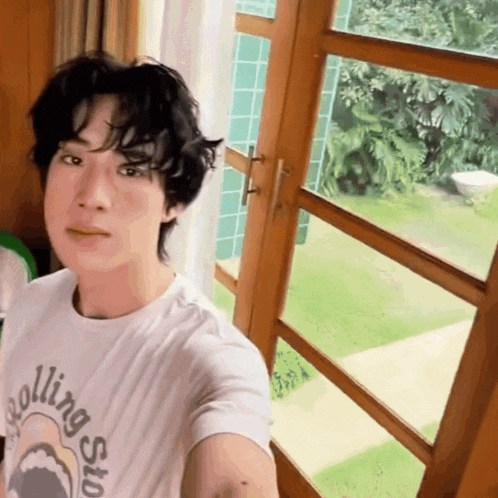 a man wearing a rolling stones shirt takes a selfie in front of a window