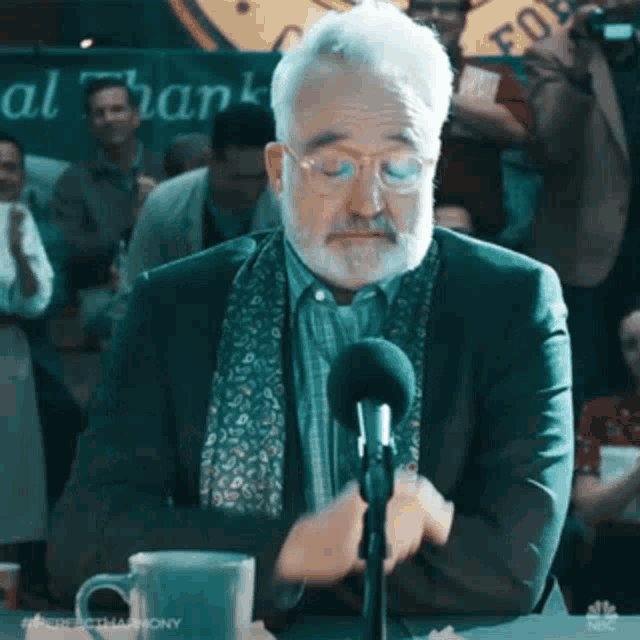a man with a beard and glasses is talking into a microphone .