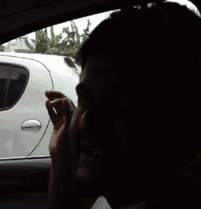 a man is smoking a cigarette while sitting in the driver 's seat of a car
