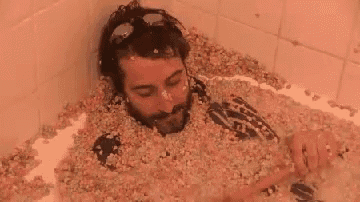 a man is laying in a bathtub filled with cereal and sprinkles .
