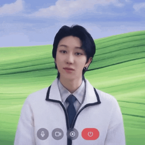 a man in a white jacket and tie is talking on a video call with a green field in the background