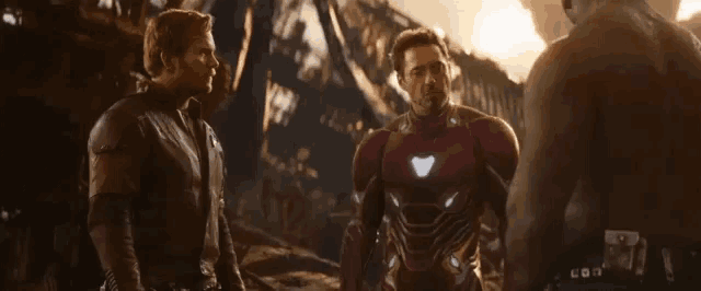 a group of men are standing next to each other and one of them is wearing a superhero suit .