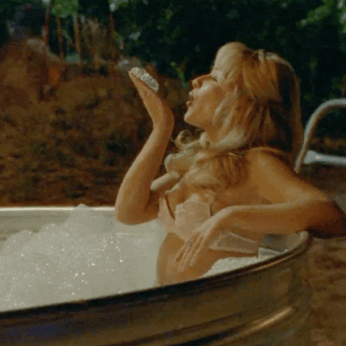 a woman is taking a bath in a metal tub and blowing bubbles