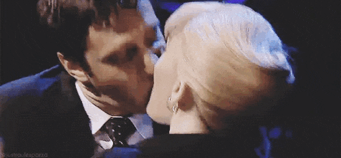a man in a suit and tie is kissing another man on the forehead .