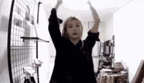 a woman in a black shirt is dancing in a room with her arms in the air .