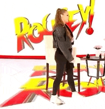 a woman is standing in front of a table and chairs in a room with a sign in the background .