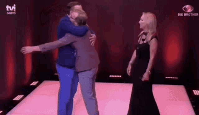 two men are hugging each other on a stage while a woman looks on .