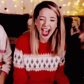 a woman is wearing a red sweater and laughing with her mouth open .