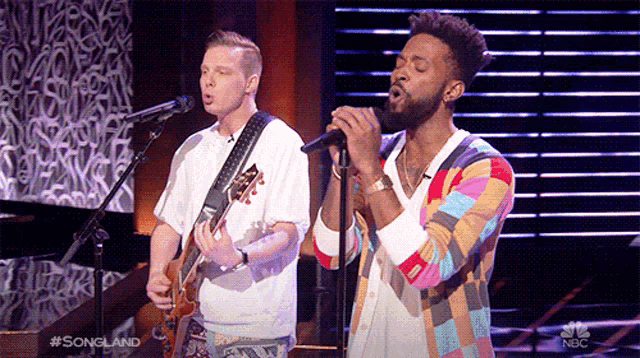 two men singing and playing guitar on a stage with a nbc logo in the corner