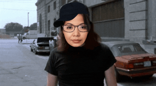 a woman wearing glasses and a black hat is standing on a street