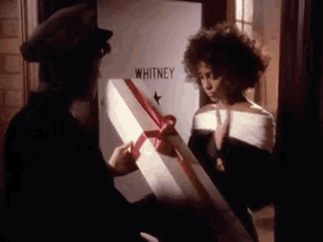 a woman is standing in front of a door holding a gift box with a red bow .