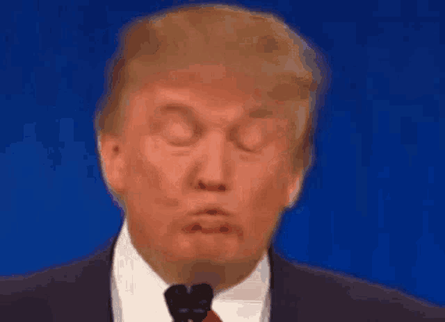 donald trump is wearing a suit and tie and making a funny face while speaking into a microphone .