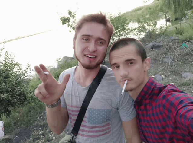 a man in an american flag shirt is smoking a cigarette next to a man in a plaid shirt