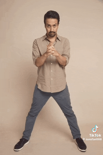 a man in a tan shirt is doing a split on a tiktok video