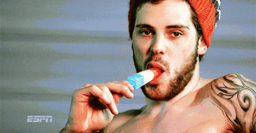 a shirtless man with a tattoo on his arm is eating a popsicle