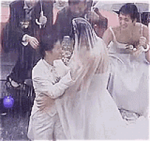 a bride and groom are hugging in the rain while their wedding party watches .