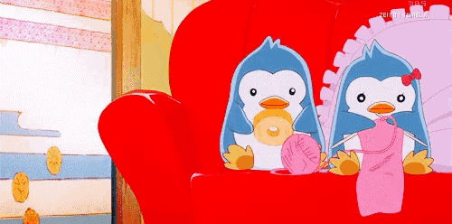 two penguins are sitting on a red couch and one is holding a ball of yarn
