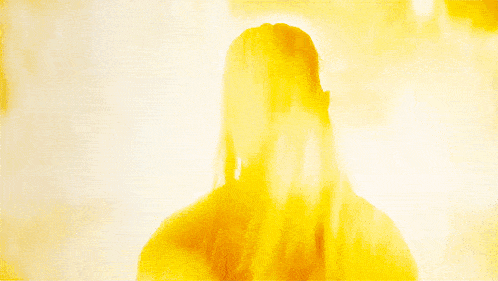 a man with long blonde hair is looking at another man in a dark room .