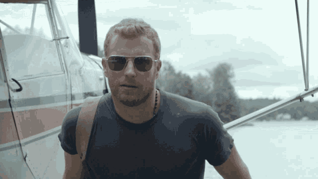 a man wearing sunglasses is standing in front of a small plane