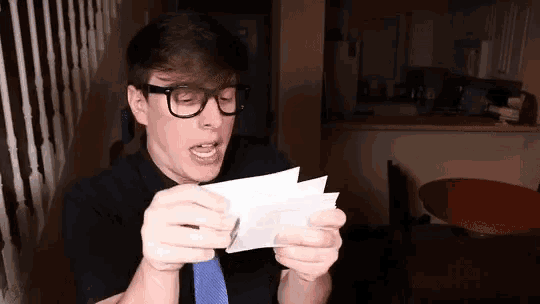 a man wearing glasses and a blue tie is holding a piece of paper in his hands
