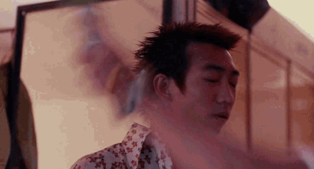 a man with a mohawk is smoking a cigarette in a room with smoke coming out of his mouth .