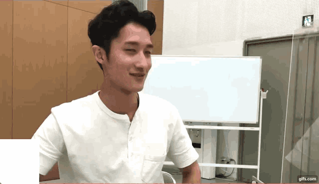 a man wearing a white shirt is sitting in front of a white board