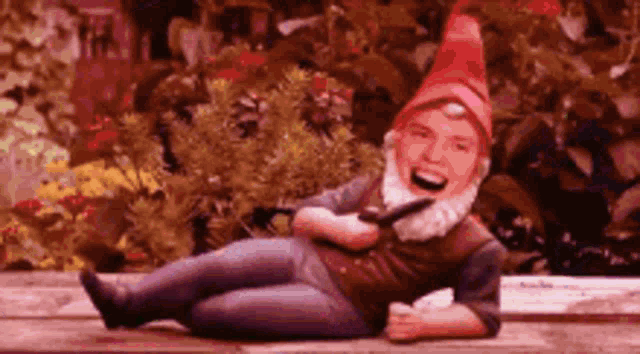 a gnome with a red hat and beard is laying down on a bench .
