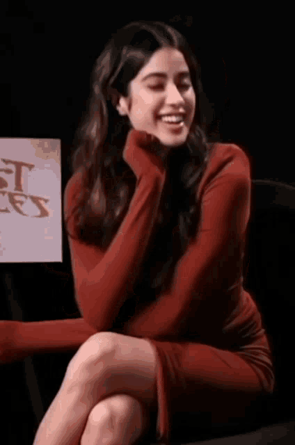 a woman in a red dress is sitting in front of a sign that says ' it 's '