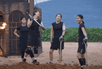a group of women standing in a dirt field with shovels