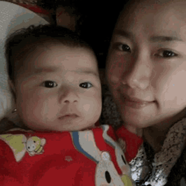 a woman is holding a baby in her arms and the baby is wearing a red shirt .