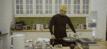 a man in a black shirt and yellow hat is cooking in a kitchen